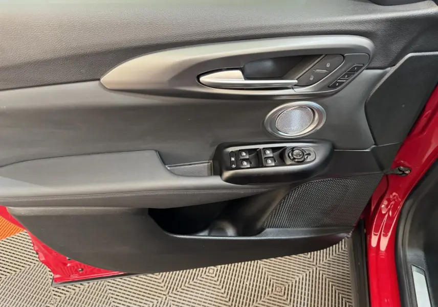Vue rapprochée de la porte avant gauche rouge de l'Alfa Romeo Tonale avec commandes électriques et haut-parleur intégré.