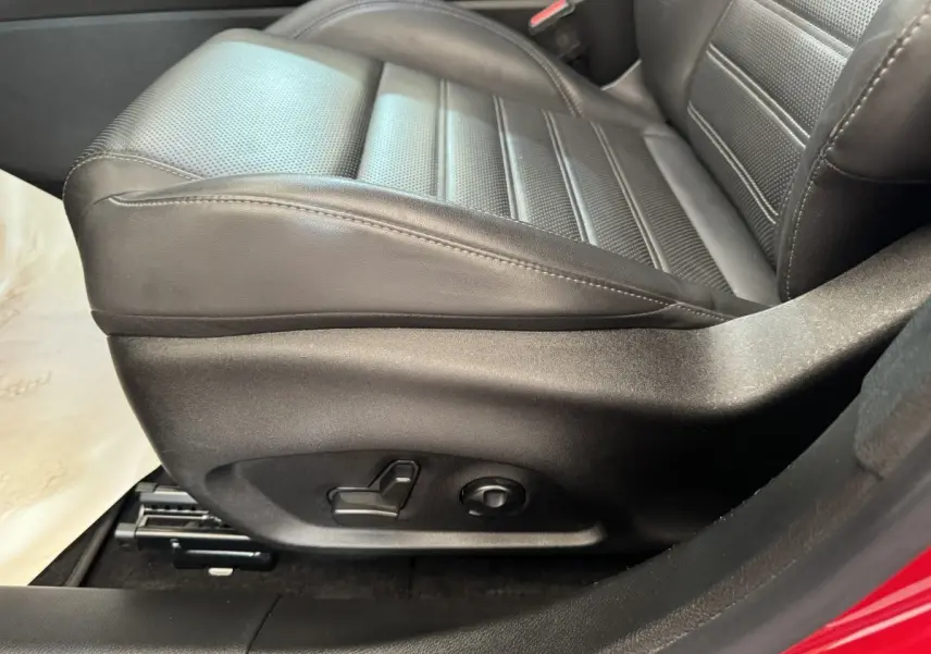 Gros plan sur le siège conducteur noir en cuir perforé de l'Alfa Romeo Tonale rouge, montrant les commandes électriques.