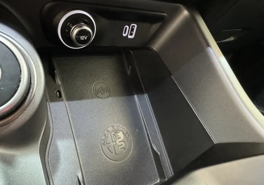Gros plan sur la console centrale noire de l'Alfa Romeo Tonale avec logo, prise 12V et port USB visible.