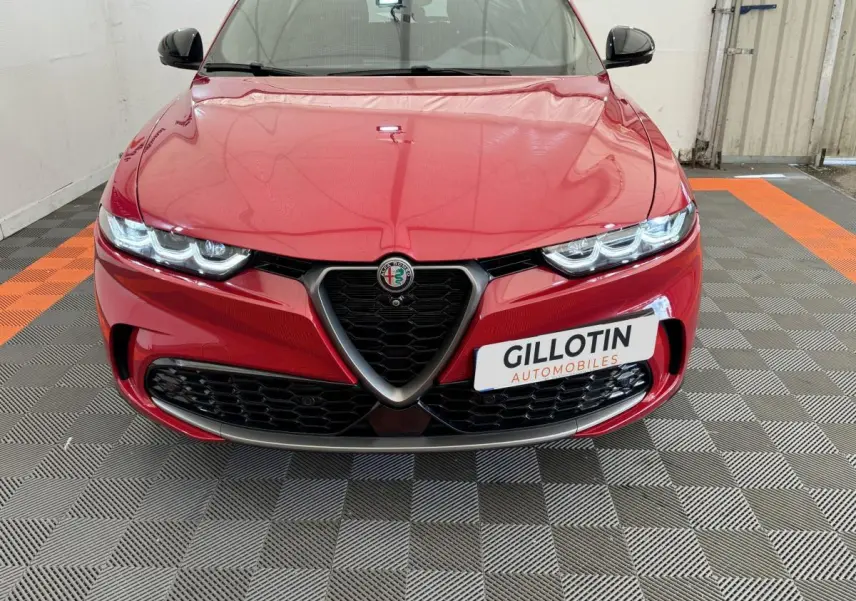 Vue frontale d'une Alfa Romeo Tonale rouge avec calandre emblématique et phares LED allumés dans un garage.