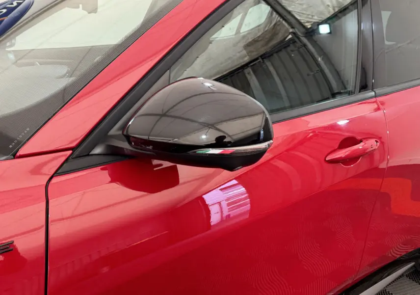 Gros plan sur la porte côté gauche rouge vif de l'Alfa Romeo Tonale avec rétroviseur noir brillant et poignée intégrée.