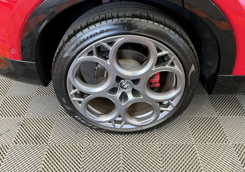 Gros plan sur la roue avant droite d'une Alfa Romeo Tonale rouge avec jante alu à cercles entrelacés et étrier de frein rouge.