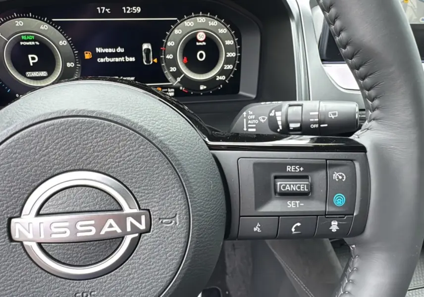 Vue rapprochée du volant cuir multifonctions Nissan Qashqai E-POWER 205 Tekna Plus avec tableau de bord numérique allumé.