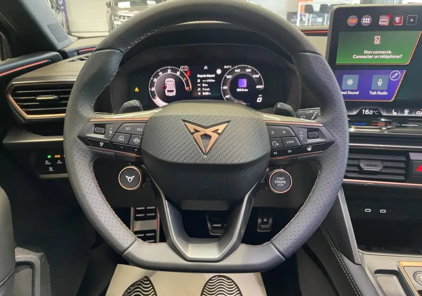 Volant CUPRA en cuir perforé avec logo cuivré, tableau de bord digital et écran tactile central dans l'habitacle noir.