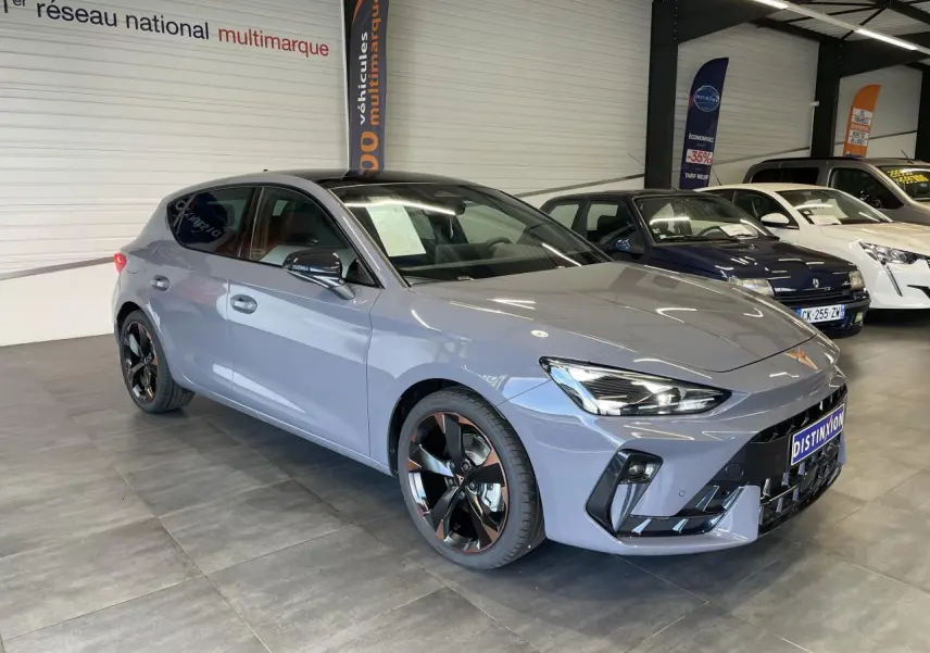 Vue 3/4 avant de la CUPRA Leon gris avec jantes cuivrées et toit ouvrant panoramique en intérieur showroom.