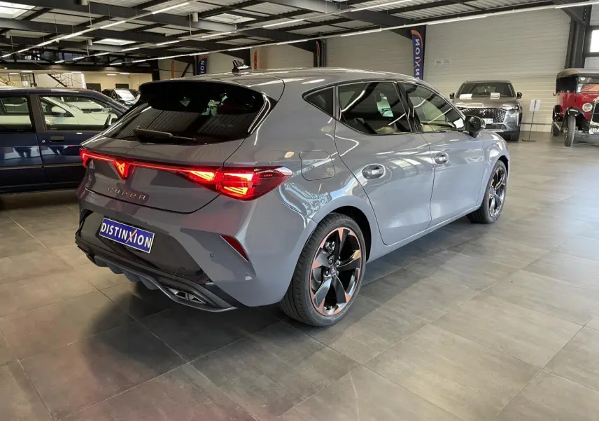 Vue 3/4 arrière droite d'une CUPRA Leon gris magnétique avec jantes cuivrées et feux arrière Tri-LED allumés.