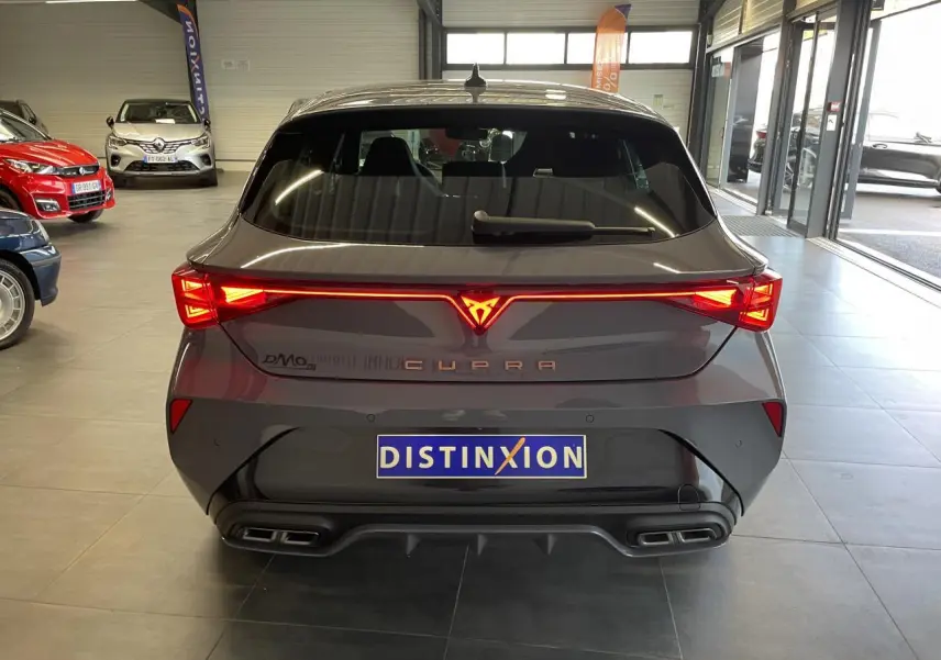 Vue arrière d'une CUPRA Leon gris magnétique avec feux arrière en bandeau lumineux et double sortie d'échappement noire.