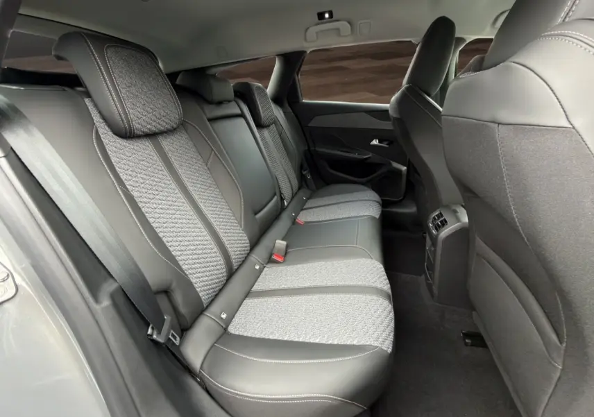 Vue intérieure arrière côté droit de la Peugeot 308 Hybrid 145 e-DCS6 Allure avec sièges gris foncé bi-matière et ceinture de sécurité.