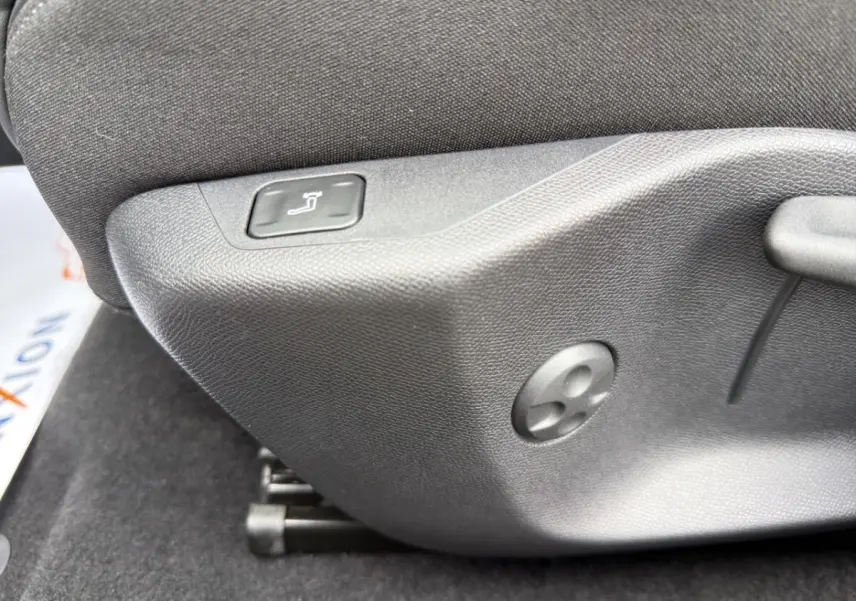 Détail de la commande de réglage manuel du siège avant en tissu gris foncé dans une Peugeot 308 Hybrid 145 e-DCS6 Allure.