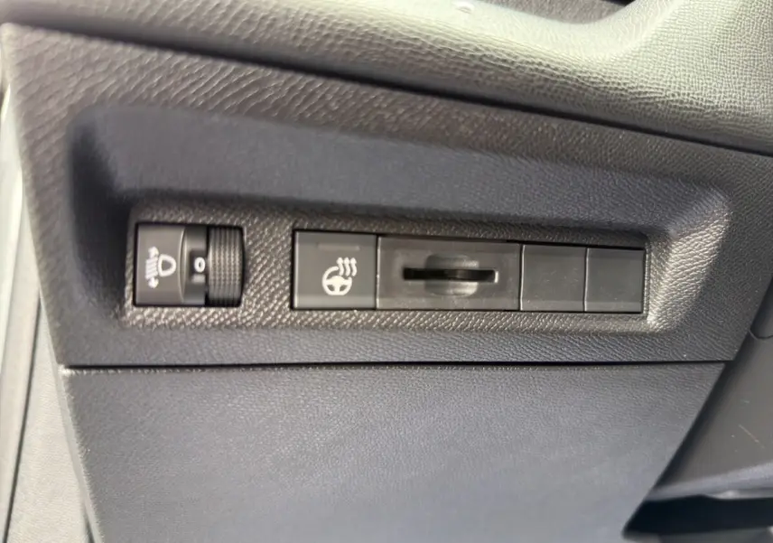 Gros plan sur les commandes de réglage des phares et du volant chauffant dans une Peugeot 308 Hybrid 145 e-DCS6 Allure.