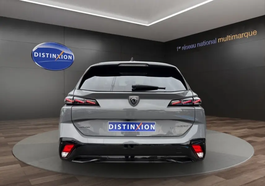 Vue arrière d'une Peugeot 308 Hybrid gris foncé avec feux LED et logo distinctif sur fond noir en showroom.