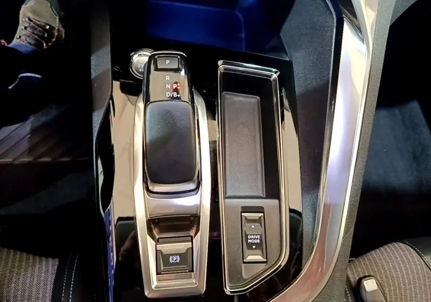 Vue rapprochée de la console centrale noire brillante du Peugeot 3008 bleu, avec levier de vitesse automatique et bouton Drive Mode.