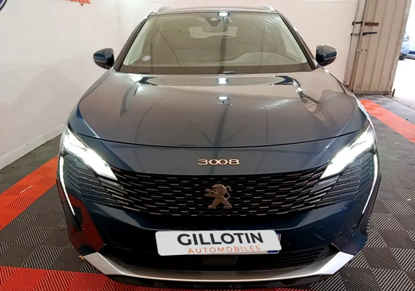 Vue avant d'un Peugeot 3008 bleu hybride rechargeable avec calandre noire et phares LED allumés dans un garage.