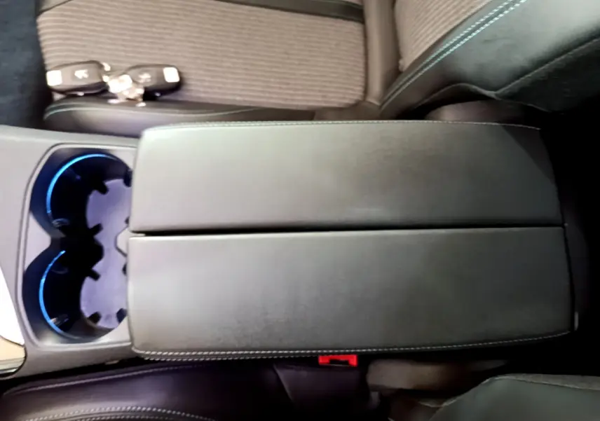 Gros plan sur l'accoudoir central en cuir noir avec surpiqûres bleues et porte-gobelets éclairés d'un Peugeot 3008 hybride bleu.