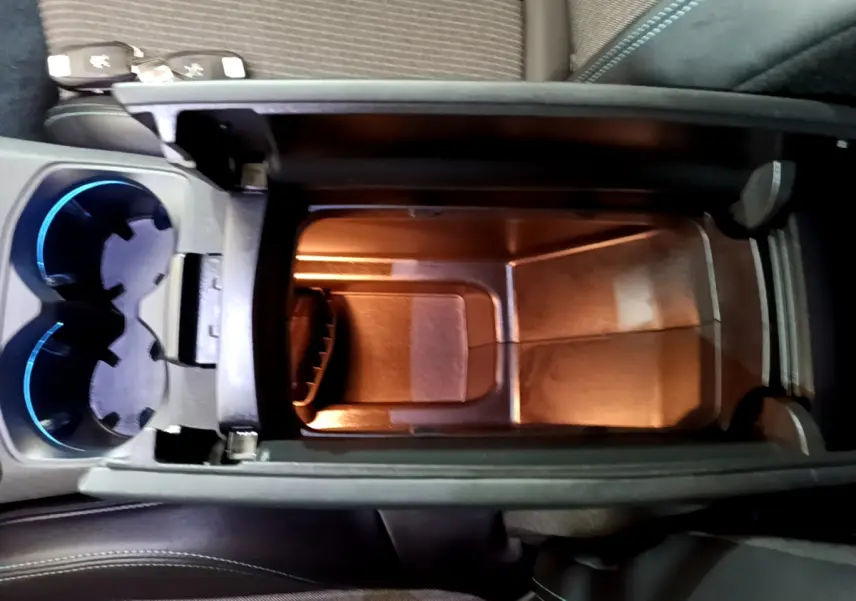 Vue plongeante sur le rangement central éclairé et les porte-gobelets bleutés du Peugeot 3008 hybride rechargeable bleu.