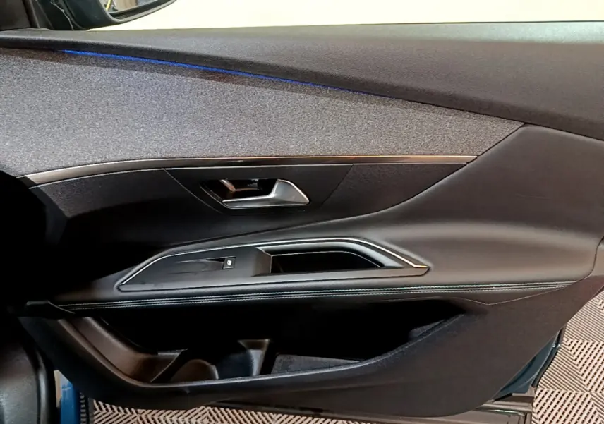 Vue intérieure côté gauche de la porte avant d'une Peugeot 3008 bleu, avec garniture noire et poignée argentée.