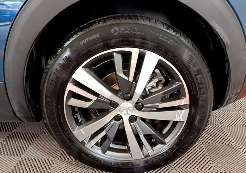 Gros plan sur la roue avant gauche du Peugeot 3008 bleu hybride, jante alliage à design moderne et pneus Michelin.