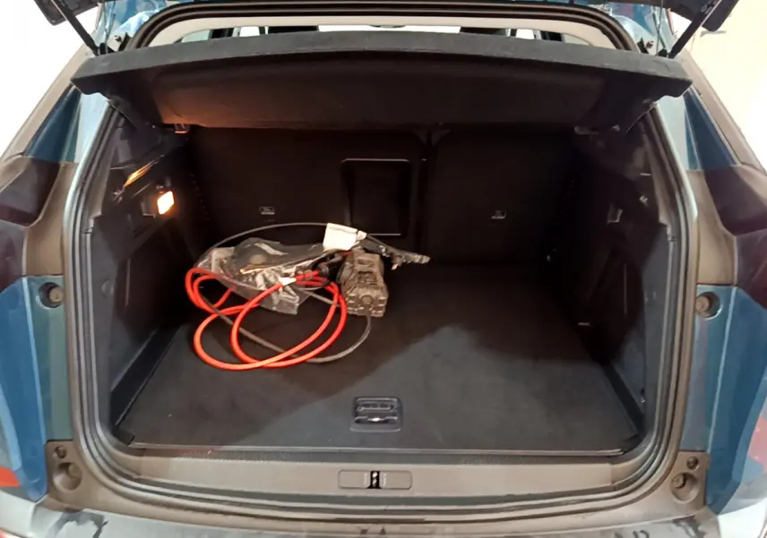 Coffre ouvert d'un Peugeot 3008 bleu hybride rechargeable, vue arrière montrant un câble de charge orange à l'intérieur.