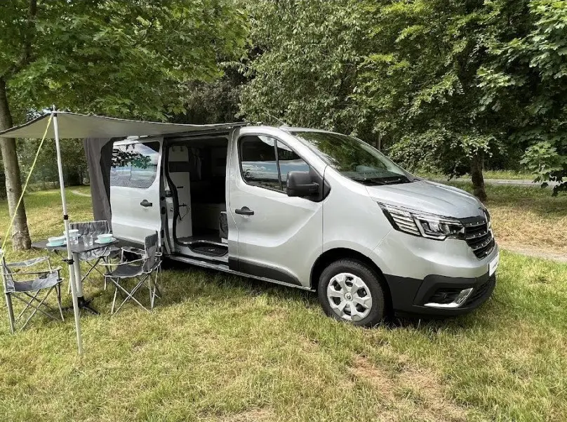 Renault Trafic Fourgon gris vue 3/4 avant droit avec porte latérale ouverte et auvent déployé en extérieur.