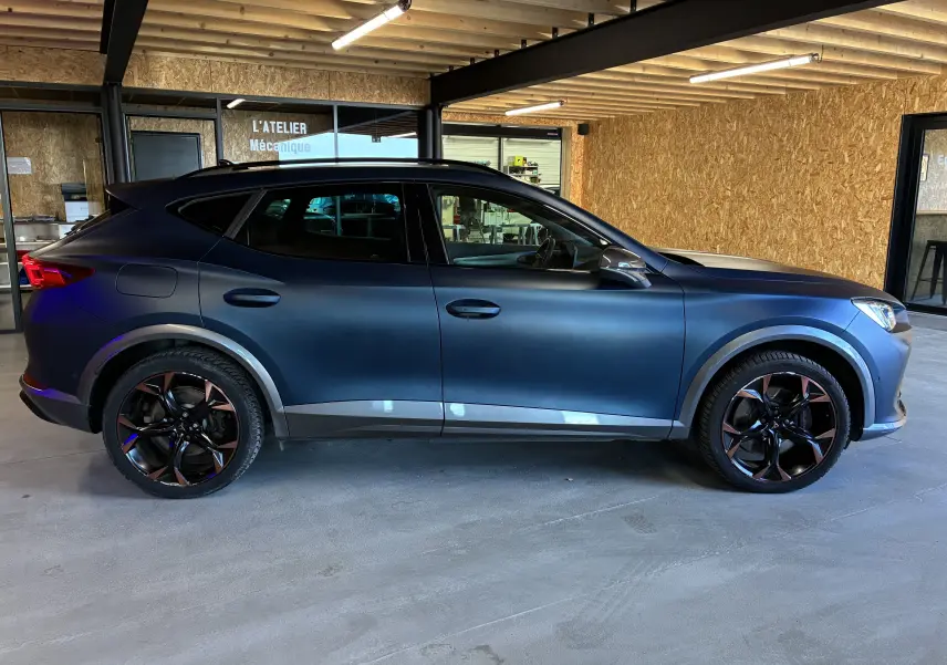 Vue de profil côté gauche d'un CUPRA Formentor bleu mat avec jantes alu noires et cuivre dans un garage.