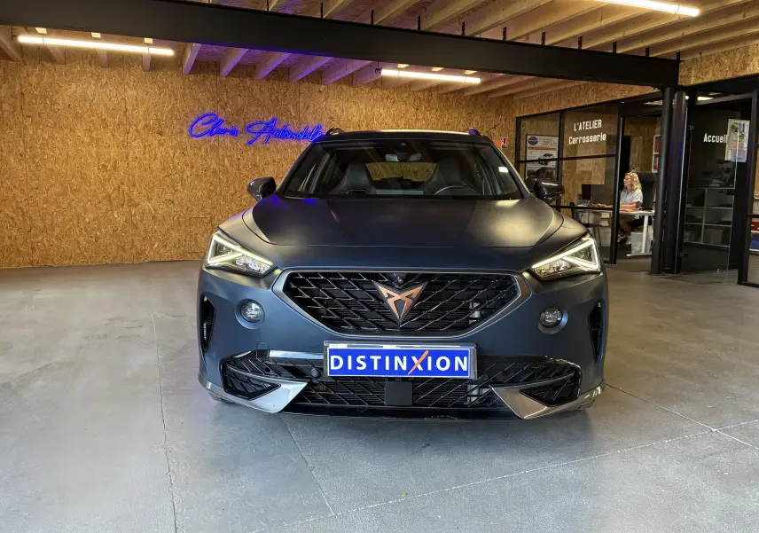 Vue frontale d'un CUPRA Formentor bleu mat avec calandre noire et logo cuivré, stationné en intérieur showroom.