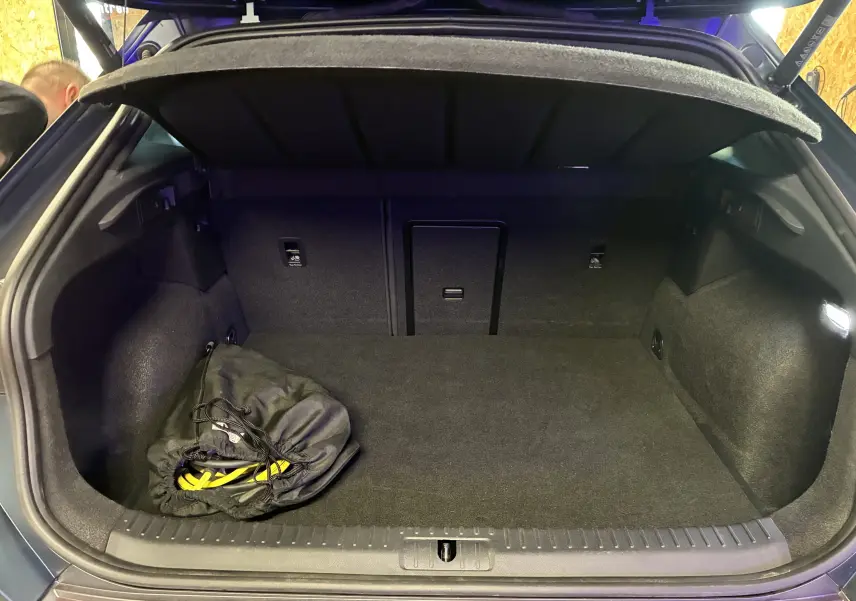 Coffre ouvert vu de l'arrière d'une CUPRA Formentor bleu, avec tapis noir et sac de câble de recharge visible à gauche.