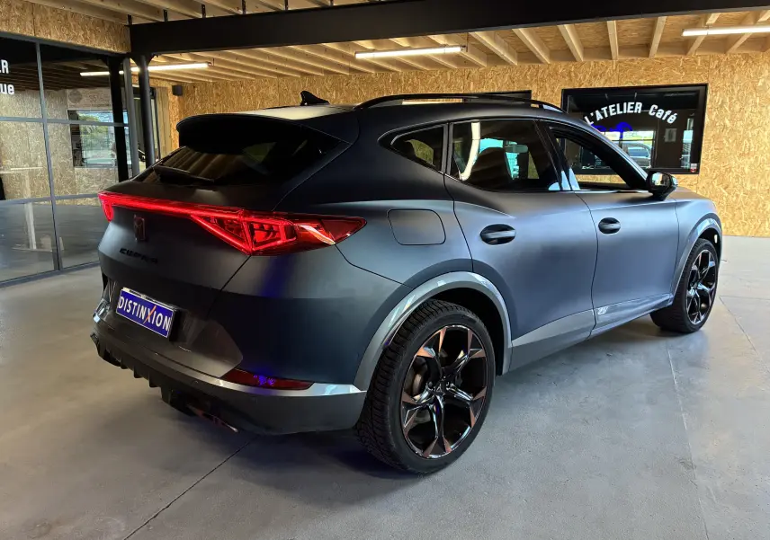 Vue 3/4 arrière droite d'un CUPRA Formentor bleu mat avec jantes alu noires et feux arrière LED allumés en intérieur.