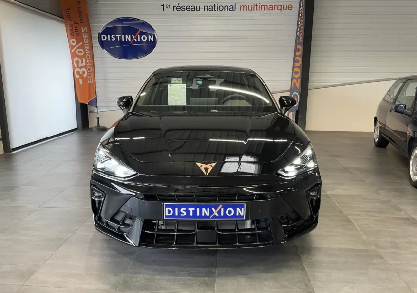Vue frontale d'une CUPRA Leon noire avec logo cuivré, phares allumés et calandre sportive en showroom.