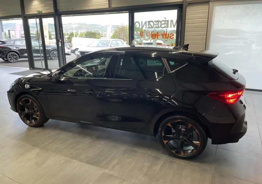 Vue de profil côté gauche d'une CUPRA Leon noire avec jantes alliage 18'' cuivrées en intérieur showroom.
