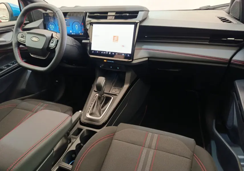 Intérieur Ford Puma 2025 vu côté conducteur, tableau de bord noir avec écran tactile central et coutures rouges sur sièges.
