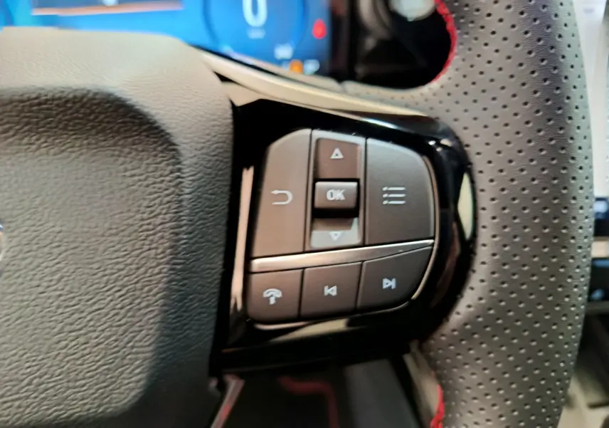 Gros plan sur les commandes multifonctions à droite du volant perforé noir avec surpiqûres rouges du Ford Puma bleu 2025.