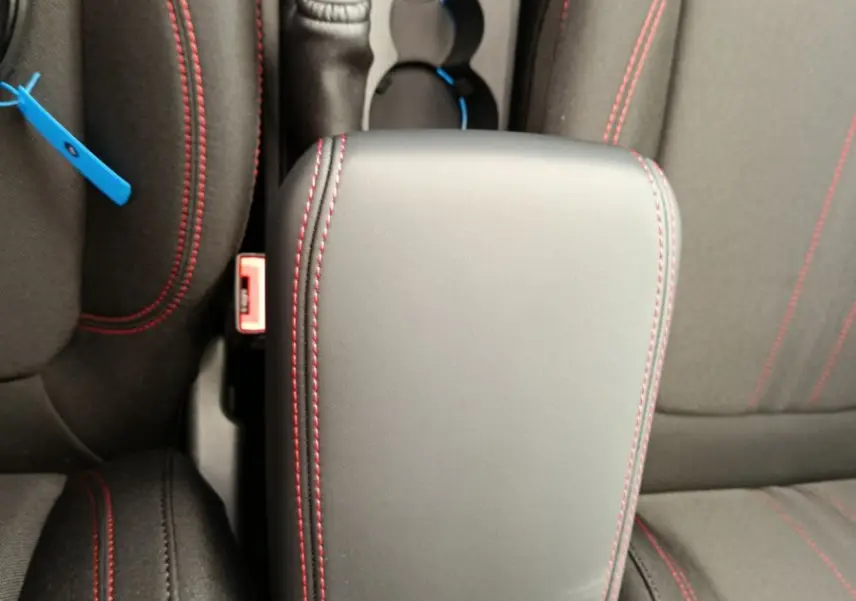 Vue plongeante sur l'accoudoir central noir avec surpiqûres rouges entre les sièges avant du Ford Puma bleu.