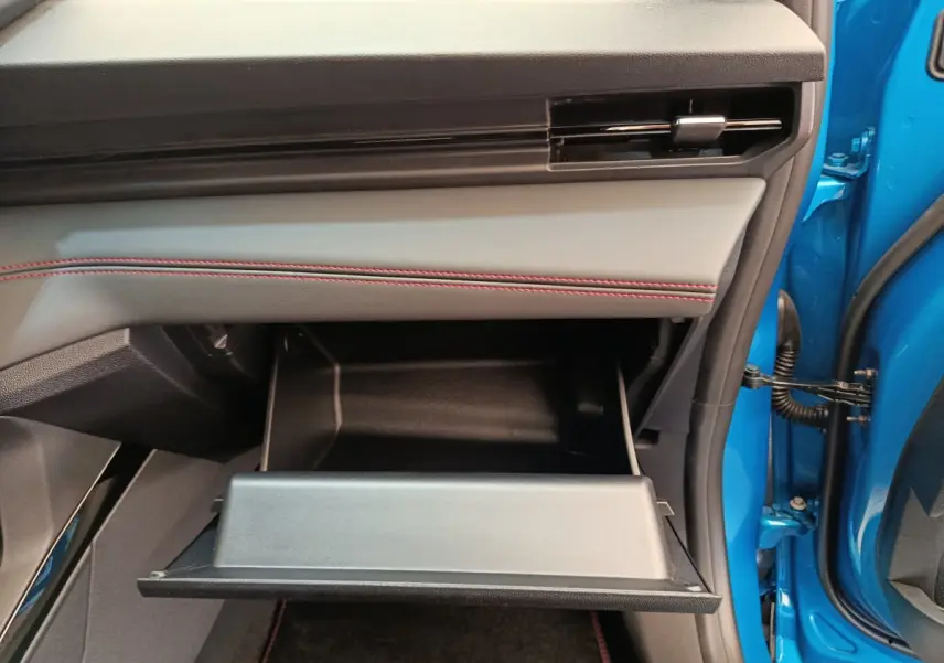 Gros plan sur la boîte à gants ouverte côté passager du Ford Puma bleu, soulignant la finition intérieure avec surpiqûres rouges.