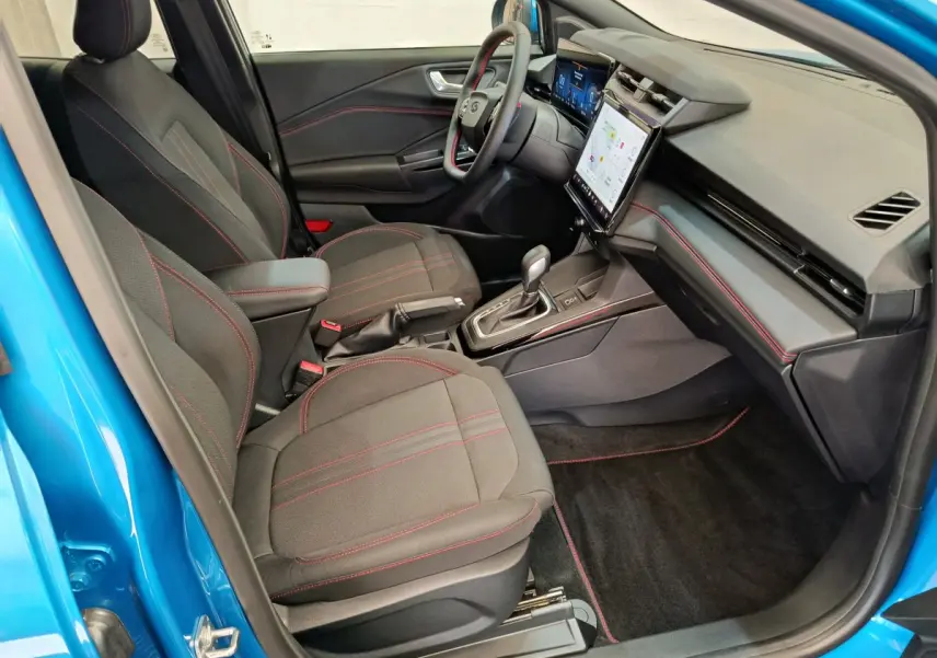 Intérieur avant droit du Ford Puma bleu 2025, sièges noirs avec surpiqûres rouges et écran tactile central visible.