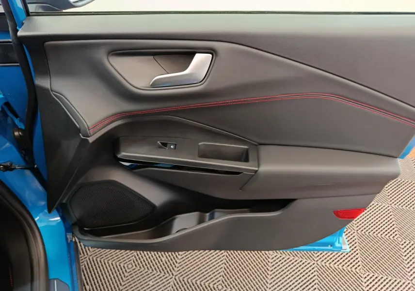 Intérieur côté gauche de la porte avant d'une Ford Puma bleu 2025 avec surpiqûres rouges et poignée argentée.
