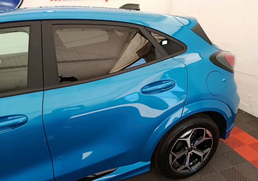 Vue côté droit arrière du Ford Puma bleu 2025 avec jante alliage et vitres teintées dans un showroom.
