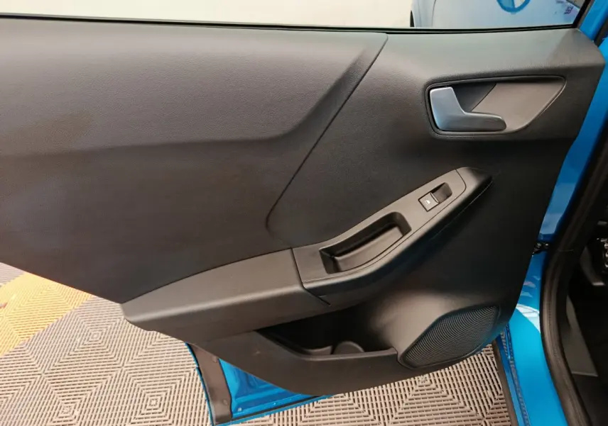 Vue rapprochée de la porte avant droite noire du Ford Puma bleu 2025, avec commande de vitre et poignée intégrée.