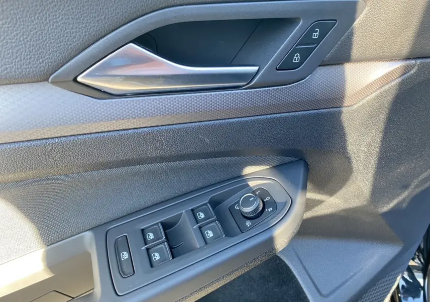 Détail de la porte côté conducteur d'une Volkswagen Golf VIII noire, montrant les commandes des vitres et rétroviseurs.