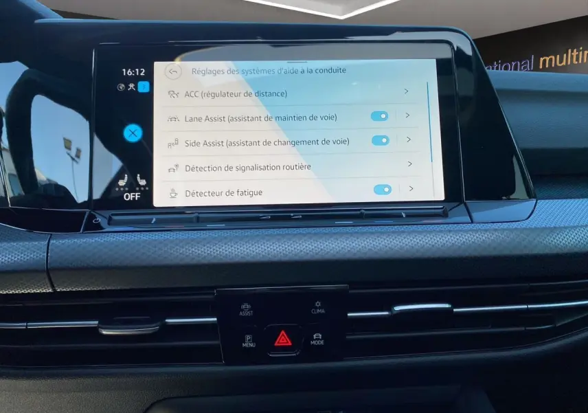 Vue rapprochée de l’écran tactile central de la Volkswagen Golf VIII noire affichant les réglages d’aides à la conduite.