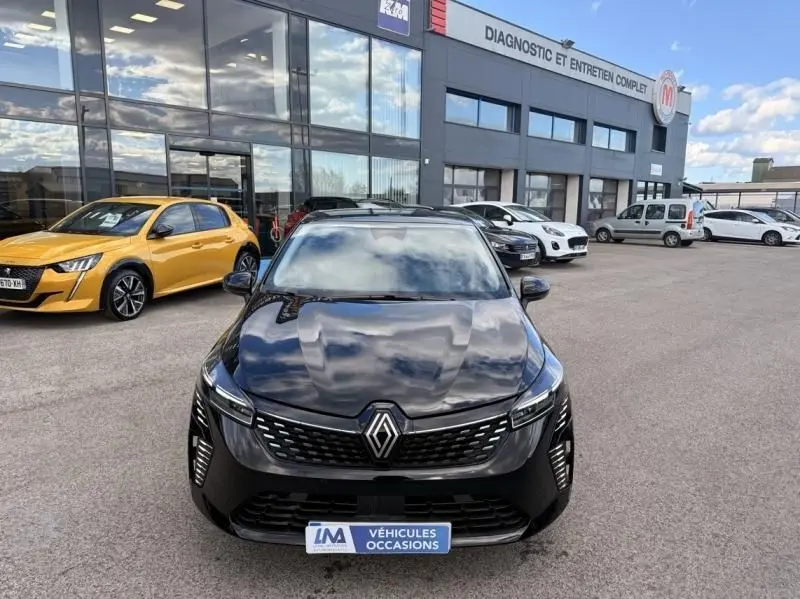 Vue avant d'une Renault Clio V noire 2025 avec calandre moderne et logo Renault bien visible, stationnée devant un garage.