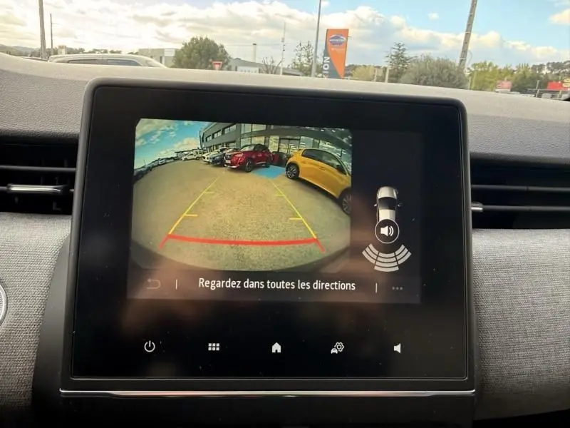 Vue de la caméra de recul de la Renault Clio V noire, affichant l'arrière et le parking avec des voitures colorées.