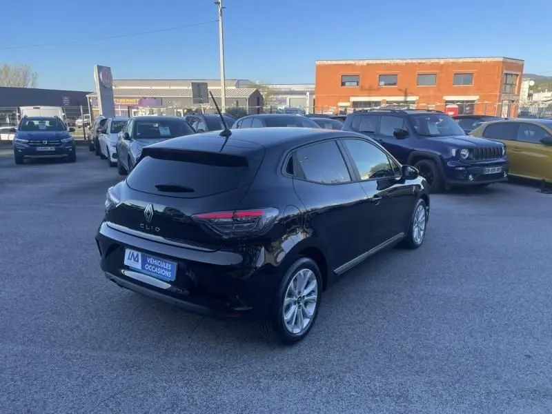 Vue 3/4 arrière droite d'une Renault Clio V noire 2025, avec feux arrière allongés et jantes argentées, stationnée en extérieur.