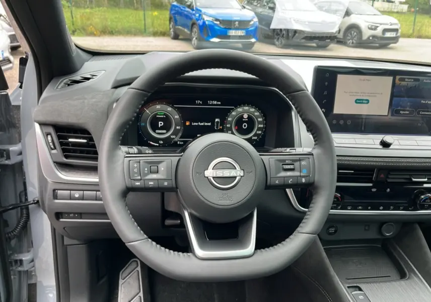 Vue intérieure centrée sur le volant cuir du Nissan Qashqai E-POWER 205 Tekna Plus gris argile avec tableau de bord numérique.