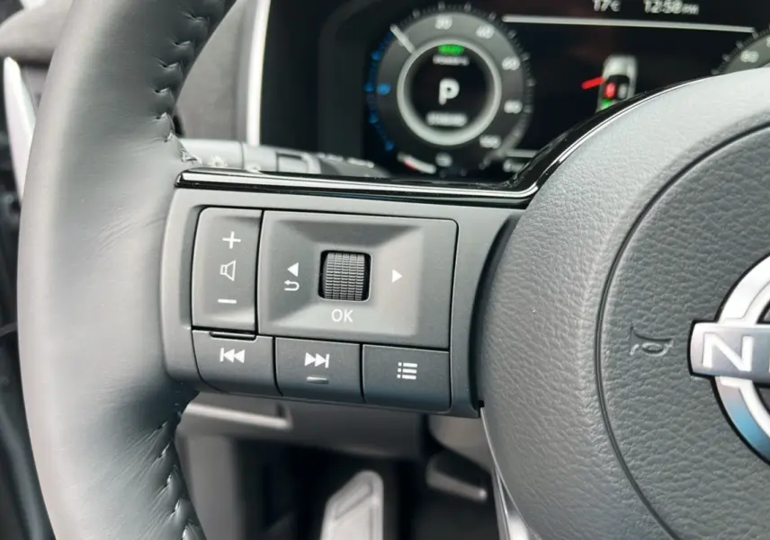 Gros plan sur les commandes gauche du volant cuir noir du Nissan Qashqai E-POWER 205 Tekna Plus avec tableau de bord numérique.