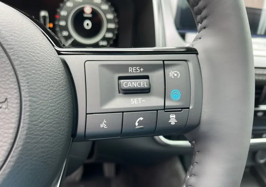Gros plan sur les commandes au volant cuir gris du Nissan Qashqai E-POWER 205 Tekna Plus, avec tableau de bord flou en arrière-plan.
