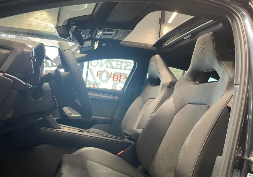 Vue intérieure côté conducteur de la CUPRA Leon 2026, sièges baquets noirs avec surpiqûres cuivrées et toit ouvrant panoramique.
