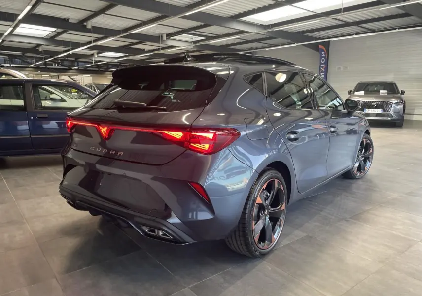 Vue 3/4 arrière droite d'une CUPRA Leon gris magnétique avec jantes alliage 18'' cuivrées et feux arrière Tri-LED allumés.