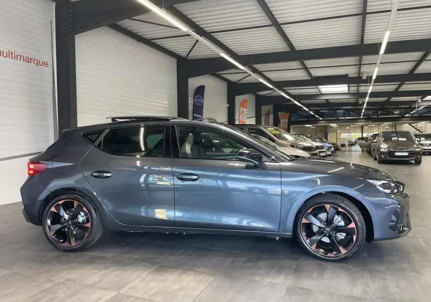 Profil droit d'une CUPRA Leon 2.0 TDI gris magnétique avec jantes alliage 18'' cuivrées en showroom.