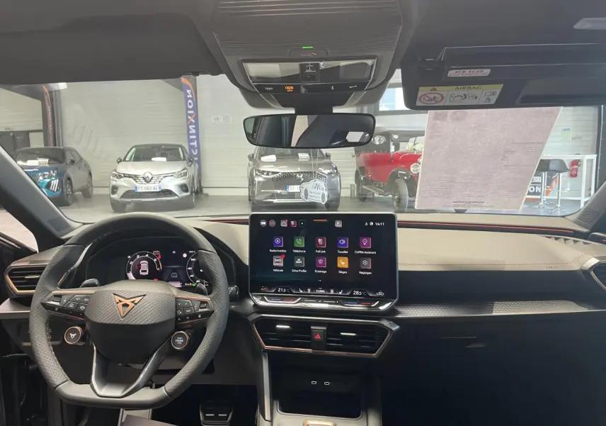 Vue intérieure frontale du tableau de bord et volant noir de la CUPRA Leon 2026 avec écran tactile central allumé.