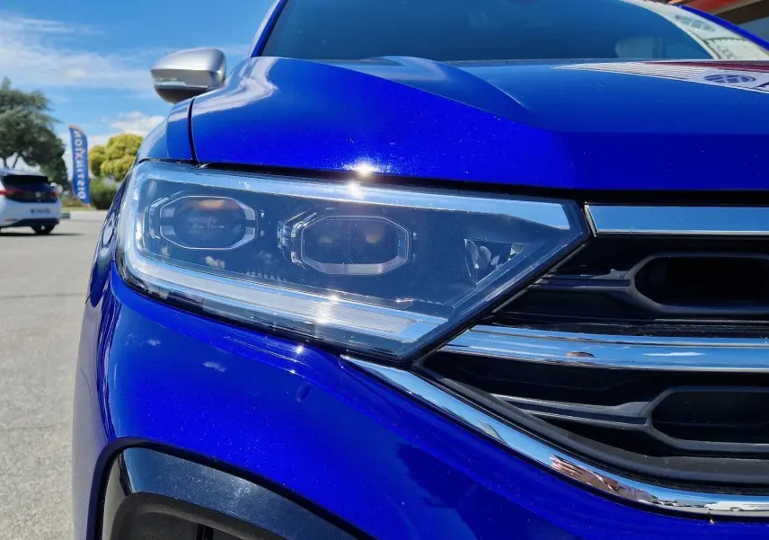 Gros plan sur l'avant gauche du Volkswagen T-Roc bleu Lapiz 2022, mettant en valeur son phare LED et la calandre chromée.